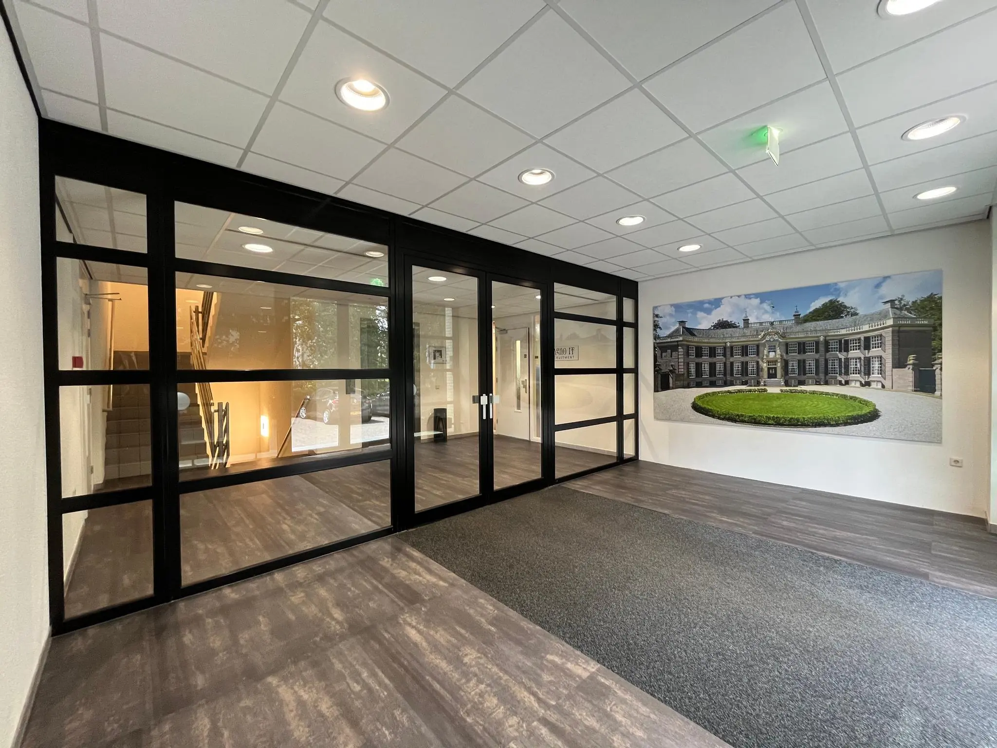 Entreehal van een modern kantoorpand aan de Oude Utrechtseweg met glazen deuren, trappenhuis en een grote foto van een klassiek gebouw aan de muur.